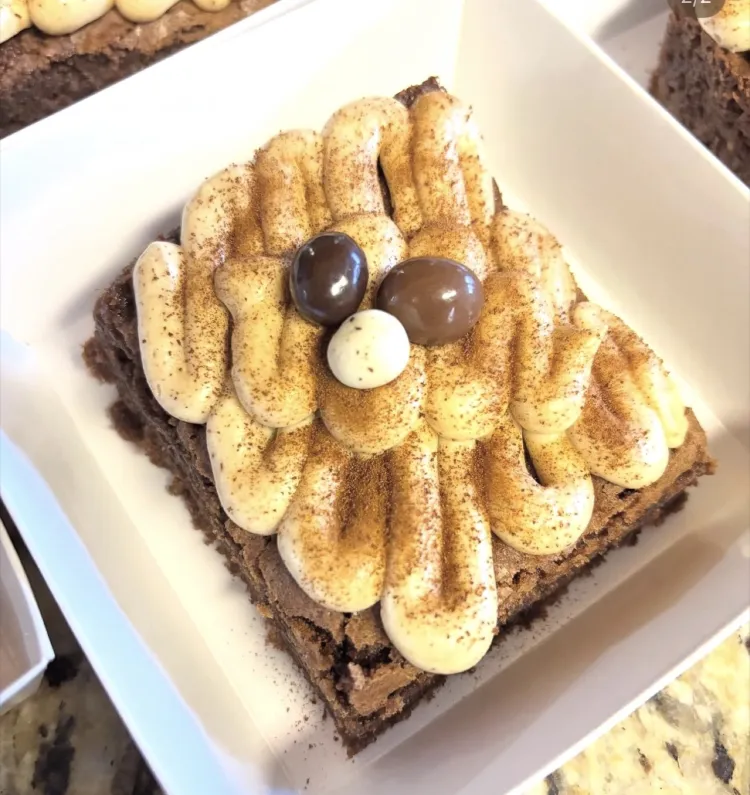 Espresso brownie topped with piped cream, cocoa, and chocolate-covered espresso beans